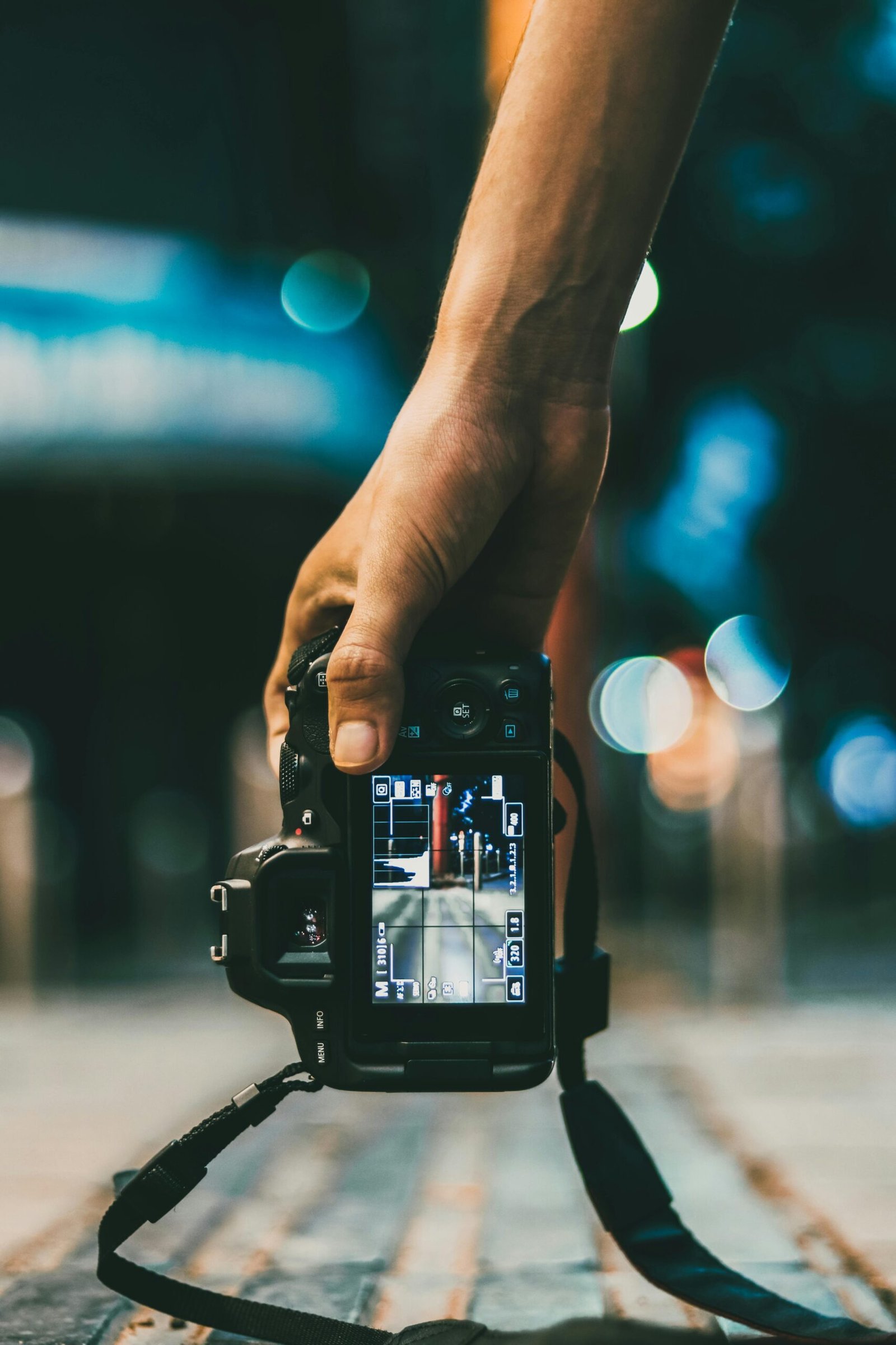 Close-up of a hand holding a DSLR camera capturing an urban night scene.